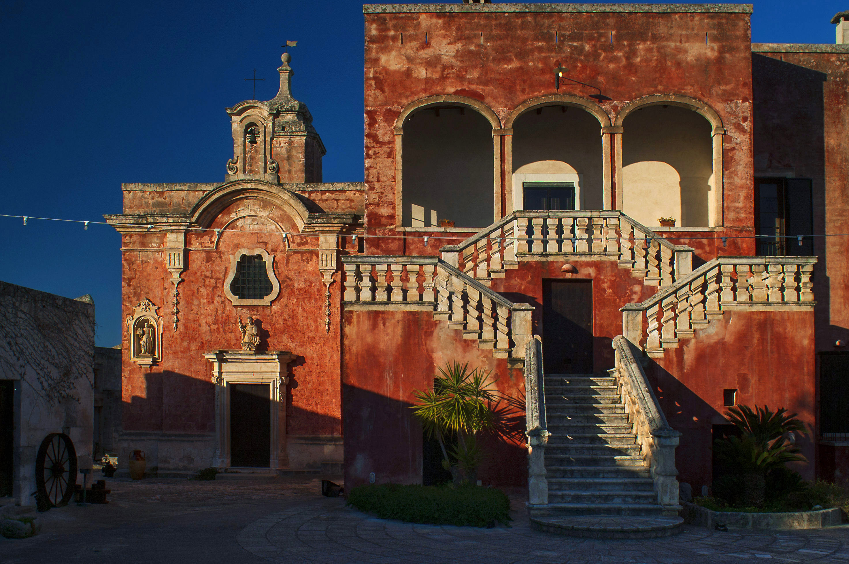 The red-washed Baroque facade and double staircase of Masseria Spina near Monopoli, Puglia, at dusk.