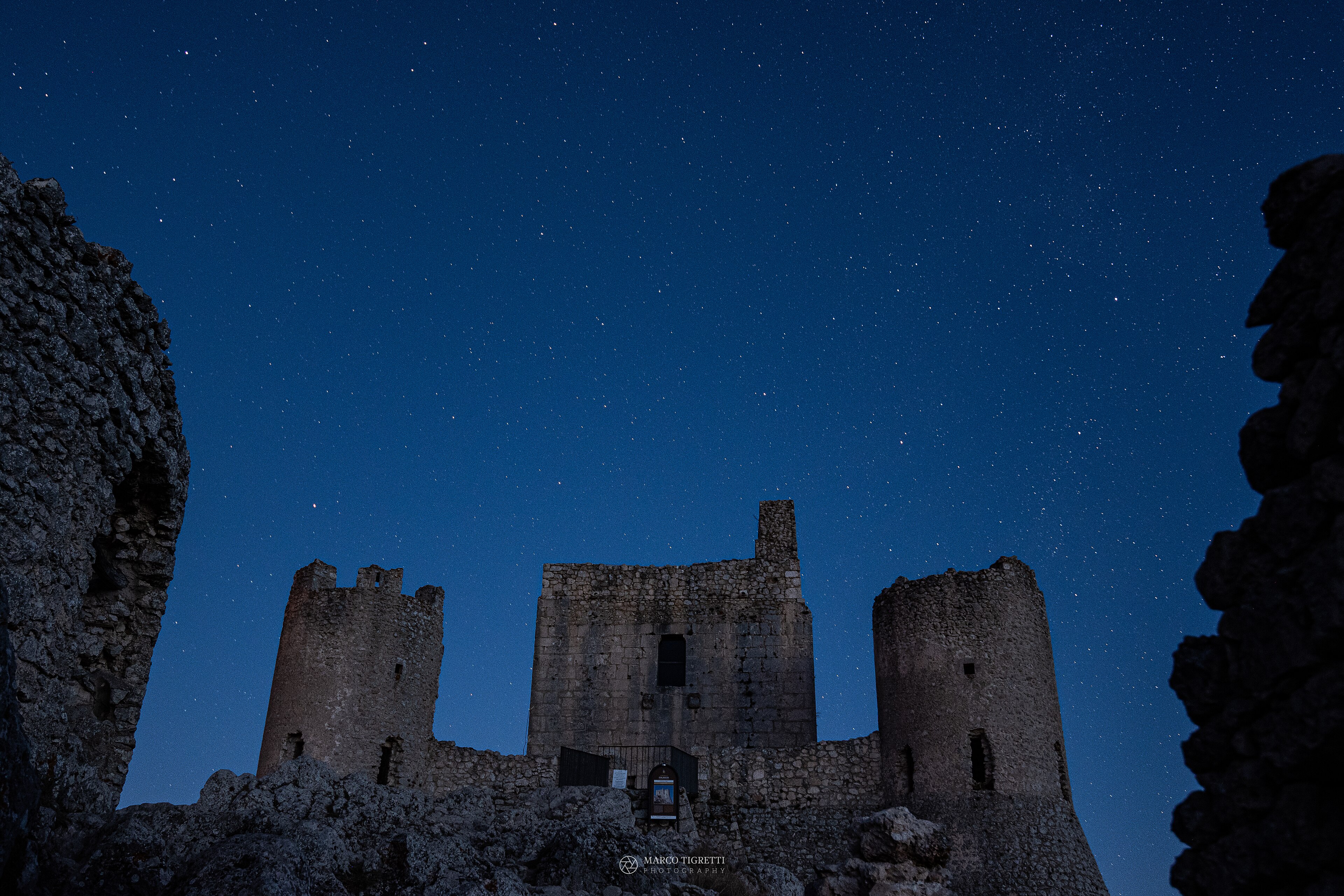 Rocca Calascio castle beneath a star-filled predawn sky in Abruzzo, Italy.
